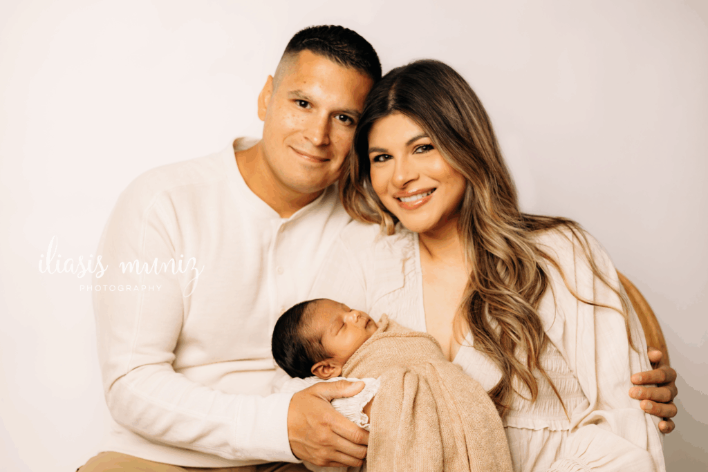 Newborn baby wrapped in a tan blanket being kissed by first-time parents during a professional studio photo session in Los Fresnos, Texas.